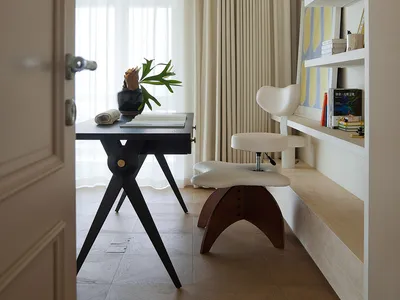 A modern home office space featuring a wooden table and a white desk chair, with a built-in bookshelf and a large window with