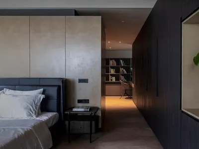 A modern, minimalist bedroom featuring dark wooden furniture and a luxurious bed setup with a black headboard and white beddi