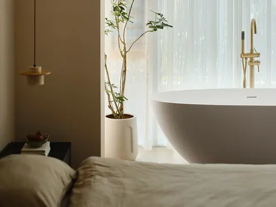A minimalist bedroom featuring a white bathtub, sheer white curtains, and light-colored fabric bedding.