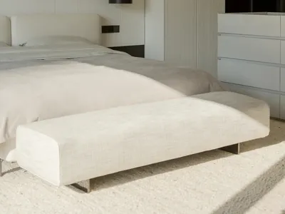 A minimalist bedroom with white furniture and a large window.