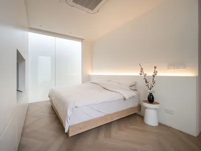 Minimalist bedroom with white bedding, wood floor, and frosted glass wall.