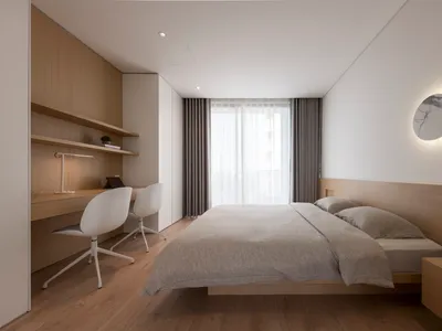 Minimalist bedroom with a wooden bed, fabric bedding, and a white chair with a desk lamp.