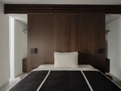 A modern minimalist bedroom with a wooden panel wall, white bedding, and a black and white striped blanket.