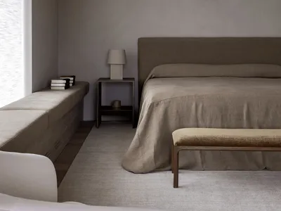 Minimalist bedroom featuring beige and wooden furniture, linen sheets, and a large window