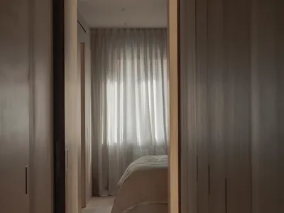 Minimalist bedroom with neutral-toned textiles and light filtering through sheer curtains.