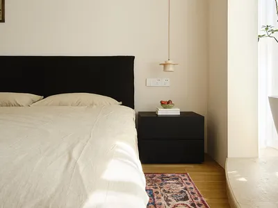 Minimalist bedroom with white walls, wooden furniture, and a bed covered in white bedding.