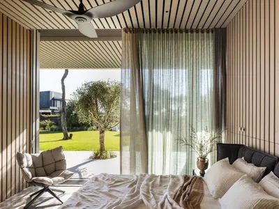 A minimalist bedroom with wooden walls, a bed, and a curtain lets in natural light.