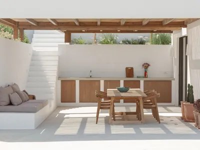 Minimalist outdoor kitchen with wooden furniture and white walls.