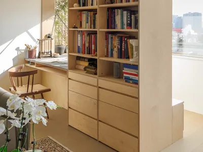 A modern home office featuring wooden shelves filled with books and storage drawers below.