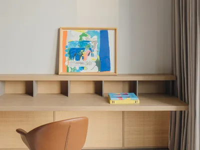 Minimalist home office with wooden furniture, a brown leather rolling chair, and a colorful abstract painting on the desk.