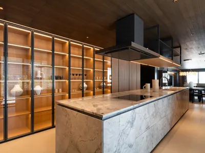 A modern kitchen with marble countertops and illuminated wooden shelving.