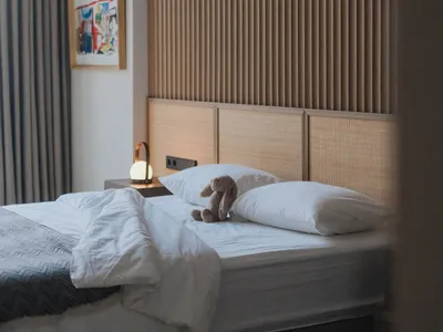 A minimalist bedroom featuring a white wooden headboard, white bedding, and a rabbit plush toy on the bed.