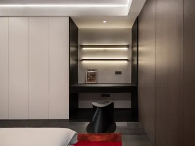 A modern minimalist bedroom with wooden walls, shelves, and a desk with a stool underneath.
