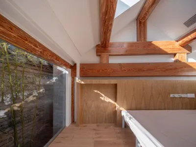 A modern minimalist bedroom featuring wooden beams and a skylight.