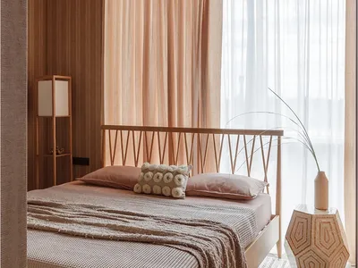 A minimalist bedroom featuring a bed with a wooden headboard and fabric bedding, surrounded by fabric curtains and a wooden f