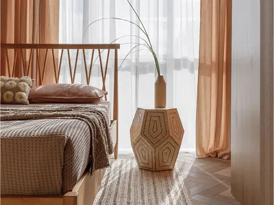 Minimalist bedroom with light-colored wooden frame, fabric bedding, and glass vase