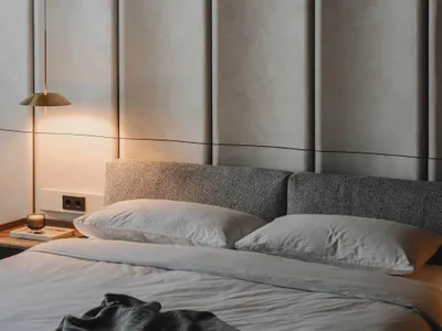 Modern bedroom featuring grey fabric bedding and a grey upholstered headboard against a neutral wall.