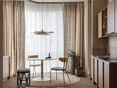 A modern kitchen with neutral tones, featuring a round table, chairs, and a potted plant under a pendant light.