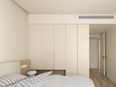 一間極簡臥室，配有白色床鋪、條紋寢具，以及白色櫃子。