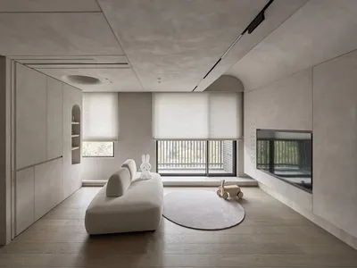 A minimalist living room interior with concrete walls and floor, featuring a white sofa, a round rug, and a child's toy on th