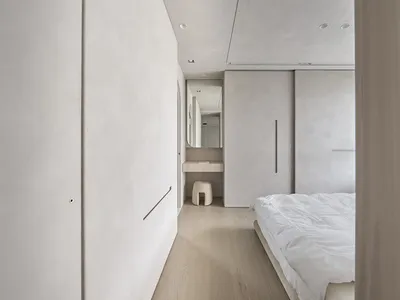 一間當代極簡臥室，擁有混凝土牆面、自然木地板與簡約白色家具。