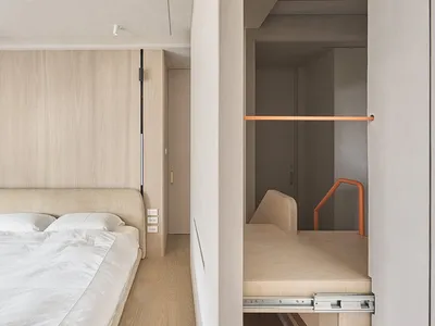 A modern minimalist bedroom with a bed against the wall and a pull-out storage unit.