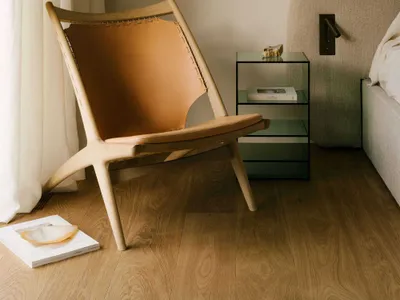 A minimalist bedroom featuring a wooden frame, leather upholstered lounge chair, and a glass top bedside table.