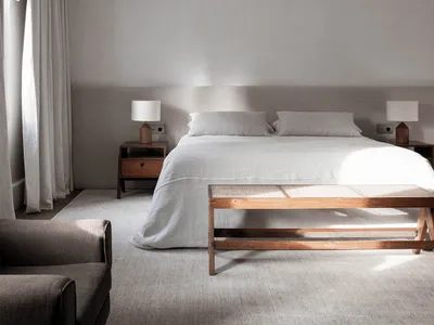 A minimalist bedroom featuring a large bed with linen bedding and wooden furniture.