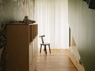 Minimalist bedroom with wooden furniture, including a wooden chair and a wooden dresser with shelves.