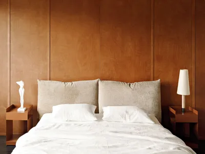 A minimalist bedroom with white bedding, gray headboard, and paneled wood walls