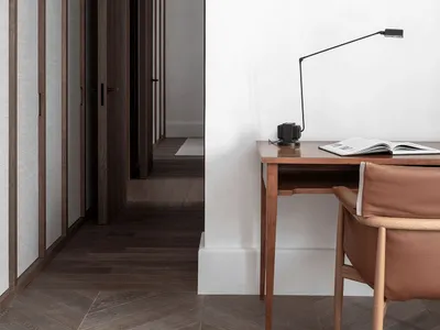 A minimalist home office with a wooden desk, leather chair, and metal desk lamp.