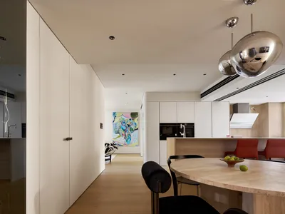 A minimalist residential kitchen with white cabinetry and wooden flooring.