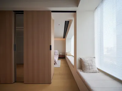 A modern bedroom featuring a window seat with cushions, wooden cabinets, and a minimalist window treatment.