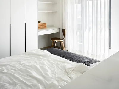 A minimalistic bedroom with a bed, sheer curtains, and a desk.