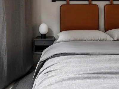 A minimalist bedroom with a brown-leather headboard, light gray bedding, and a gray curtain.