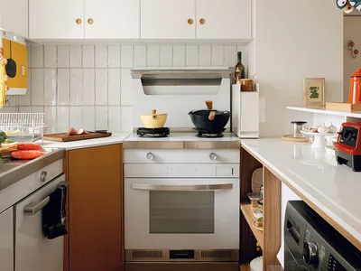 A modern, minimalist kitchen with white cabinets and a wooden floor.