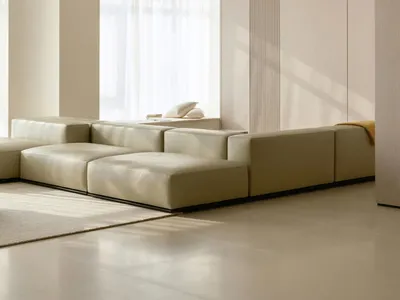 A modern minimalist living room with a large beige sectional sofa and a light-colored rug, featuring soft, neutral tones and