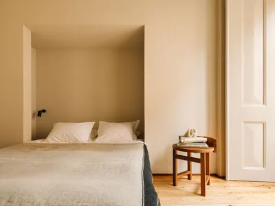 A minimalist bedroom in neutral tones with a bed, side table, and door.
