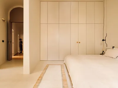 Modern minimalist bedroom with white wood flooring, cream color paneling on the wall, a single white bed with a headboard and