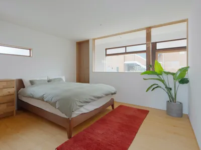 A minimalist bedroom with a bed covered in cream-colored bedding on a wooden frame, situated in a room with white walls and a