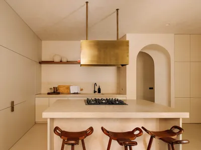 Minimalist kitchen with concrete countertops, wood stools, and industrial brass vent hood