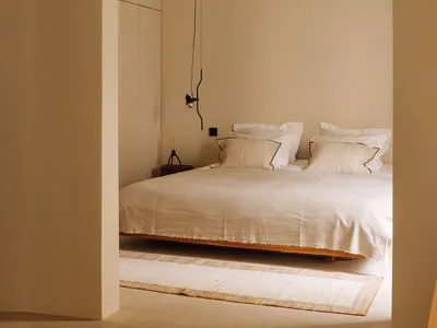 A minimalist bedroom with a white bed covered in soft textiles and wooden flooring.