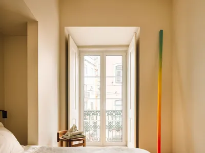 A minimalist bedroom with a bed, nightstand, and window overlooking a residential area.