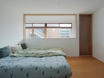 Minimalist bedroom with white walls, wooden floor, and a bed with green and blue bedding.