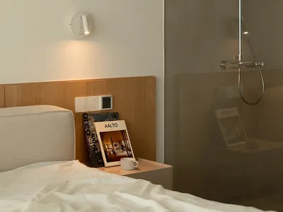 A modern minimalist bedroom with a wooden headboard and a glass-enclosed shower.