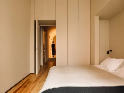 A minimalist bedroom with a bed, pillows, and a large cabinet on a wooden floor.