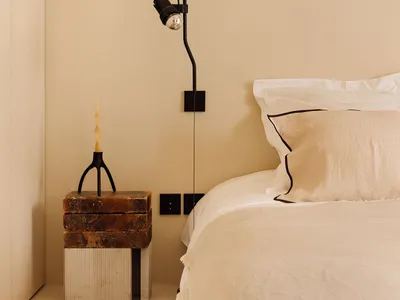 A modern bedroom with neutral tones, minimalist design, and a cozy atmosphere. Includes a bed with white bedding, a stone nig