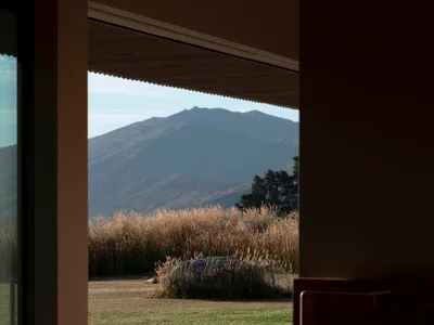 現代住宅臥室，配有大型窗戶，眺望青草田野與遠方山景。