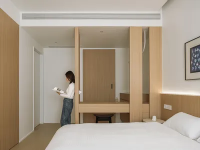 Person standing in minimalist bedroom with wood and white decor, reading a book.