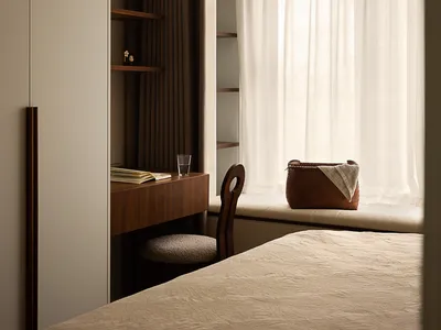 A minimalist bedroom with a bed, a chair, a desk, and a window with sheer curtains.